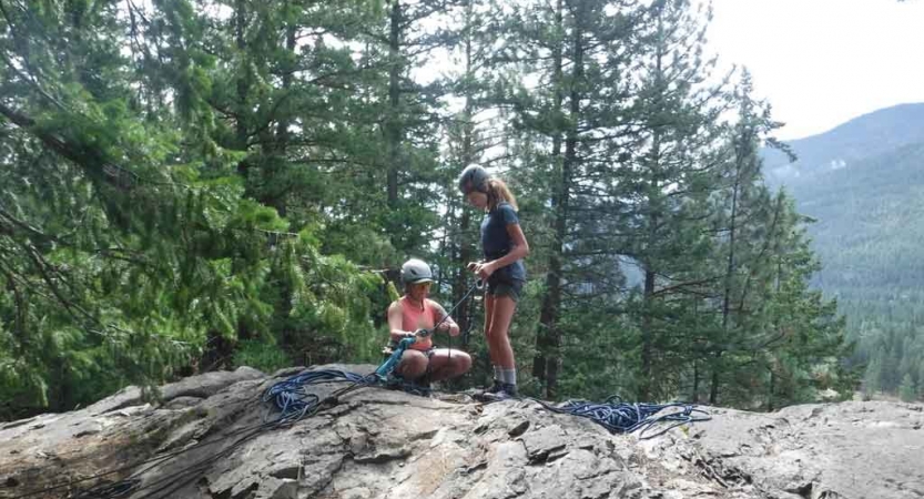 an outward bound instructor gives direction to a student preparing to rock climb